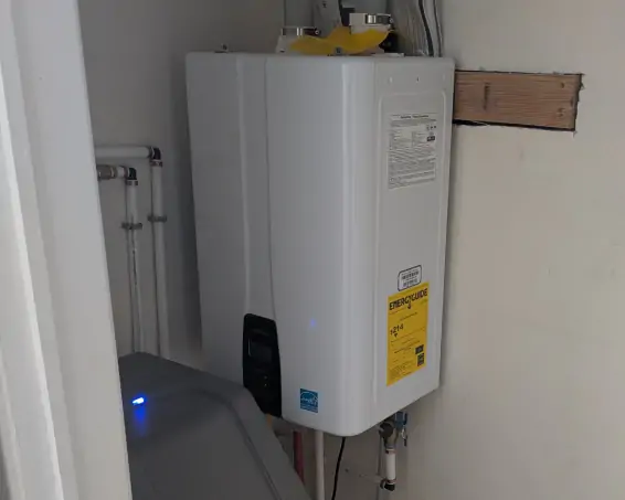 Wall-mounted tankless water heater installed beside a water softener in a utility closet